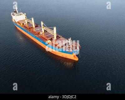 Hochwinkel-Drohnenaufnahme eines leeren Massengutschiffs, das im Winter im tiefblauen Ostseewasser schwimmt. Stockfoto