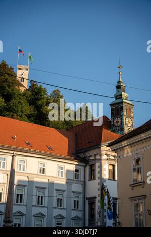 Ljubljana, Slowenien - 10. August 2025: Blick auf den Aussichtsturm der Burg Ljubljana und den Turm der Nikolaus-Kathedrale, der über dem historischen roten Dach ragt Stockfoto