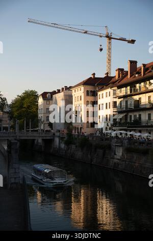 Ljubljana, Slowenien - 10. August 2025: Eine lebhafte Sommerstraße in Ljubljana, in der Menschen auf einem kopfsteingepflasterten Flussweg schlendern Stockfoto