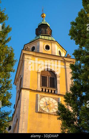 Diese vertikale Tiefwinkelaufnahme zeigt einen gelben barocken Kirchturm mit Zifferblatt und grünem Turm, der eine klassische europäische Szene einnimmt. Eingerahmt von l Stockfoto