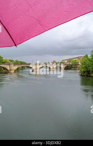Regnerischer Blick auf den Fluss Ebro und die Puente de Piedra in Logrono, La Rioja, Spanien, mit einem rosa Regenschirm im Vordergrund und bedecktem Himmel Stockfoto