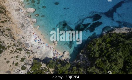 Aus der Vogelperspektive auf das türkisfarbene Meer, das die zerklüftete Küste küsst, wo sonnenverwöhnter Sand auf üppige grüne Klippen trifft, ein malerischer Kontrast, der von oben sichtbar ist Stockfoto