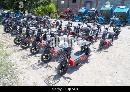Erschwingliche Elektroroller und kleine Elektrowagen parken ordentlich auf einem hellen, sonnigen Außenparkplatz in der Nähe eines Gebäudes in Sokuluk, Kirgisistan - 23. Juni 2024 Stockfoto