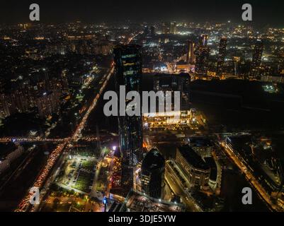Aus der Vogelperspektive auf die pulsierenden Arterien der Stadt, die von roten und weißen Lichtströmen pulsieren, die sich den dunklen Silhouetten der hoch aufragenden Gebäude gegenüberstellen. Stockfoto