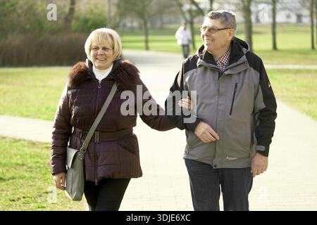 Fröhlicher Spaziergang, lebhafte Zweisamkeit, älteres Paar, das Arm in Arm in Arm in einem Park geht, sonnigen Wintertag genießt, Glück, Senioren, die Arme verbinden, Ehefrau Takin Stockfoto