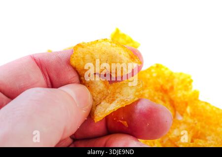 Die Hand einer Person, die ein Fragment eines knusprigen Kartoffelchips hält, mit mehr Chips im Hintergrund Stockfoto