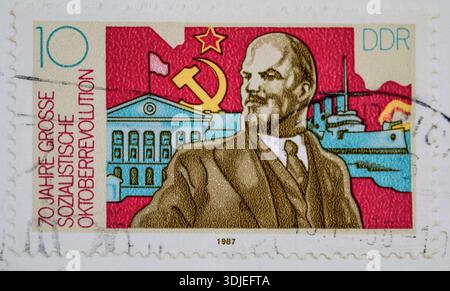 Die 1987 von der DDR erscheinende 10 Pfenninger Briefmarke erinnert an den 70. Jahrestag der Großen Oktoberrevolution. Das Design zeigt ein markantes Porträt von Wladimir Lenin neben Hammer und Sichel, ein stilisiertes Gebäude und ein Kriegsschiff vor einem leuchtend roten Hintergrund. Der Stempel trägt die deutsche Inschrift „70 Jahre große Oktoberrevolution“ Stockfoto