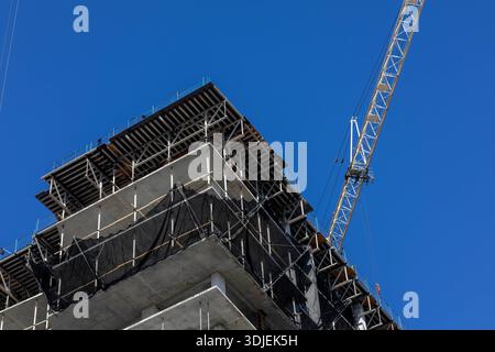 Ein professionelles, flaches Architekturbild eines mehrstöckigen Hochhauses unter aktiver Konstruktion. Das Bild zeigt einen markanten blauen Turm Stockfoto
