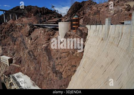 Staumauer und Stromleitungen am Hoover Dam an der Grenze zu Nevada Arizona in den USA über steilen Felsklippen und einem Versorgungsgebäude unter blauem Himmel. Stockfoto