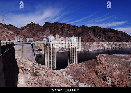 Weite Sicht auf die Ansaugtürme des Hoover Dam und das Stauwasser an der Grenze zu Nevada Arizona, USA, mit Übertragungstürmen und felsigem Gelände bei Tageslicht. Stockfoto