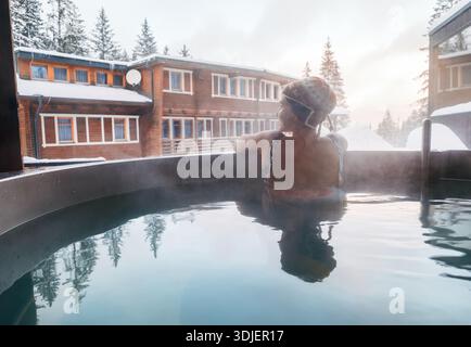 Junge Frau, die sich in Hot Water Jacuzzi im Freien Badewanne im Winter Wald Wellness Hotel und genießen angenehme gesunde Körperpflege Temperatur Behandlungen Stockfoto