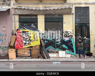 Die Straßenszene in Athen zeigt Graffiti, verworfene Poster und urbanen Verfall. Eine Person läuft an der Ladenfront vorbei. Stockfoto