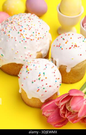 Köstliche Osterkuchen, Eier und Tulpen auf gelbem Hintergrund, Nahaufnahme Stockfoto