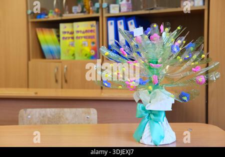 Einzigartiger Blumenstrauß aus recyceltem Kunststoff mit bunten Blumen und Dekorationen, der auf einem Holztisch in einem Klassenzimmer platziert wird und den Öko-Frien betont Stockfoto