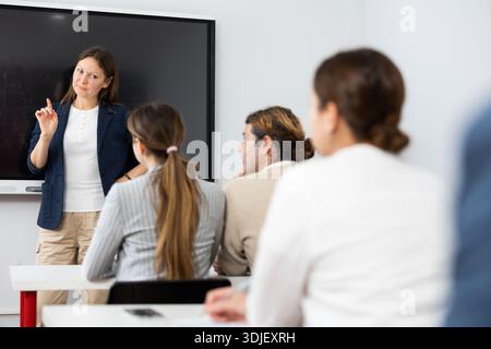 Freundliche Geschäftsfrau, die in der Nähe eines interaktiven Bretts steht und mit einer Gruppe von erwachsenen Schülern im Seminar in der Fortbildung kommuniziert Stockfoto