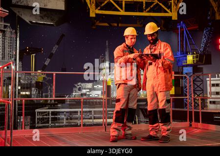 Team von Ingenieuren, die die Aktivität des Bohrgeräts bei Nacht überprüfen, um eine effiziente Öl- und Naturbrennstoffförderung von der Offshore-Plattform zu gewährleisten. Zusammenarbeit bei der Ölproduktion für die Industrie. Stockfoto
