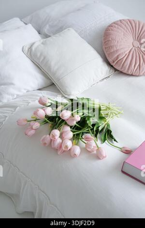Gemütliche Schlafzimmerszene mit weicher weißer Bettwäsche, dekorativen Kissen und einem lebhaften Strauß rosa Tulpen, die das ruhige Ambiente zum Entspannen unterstreichen Stockfoto