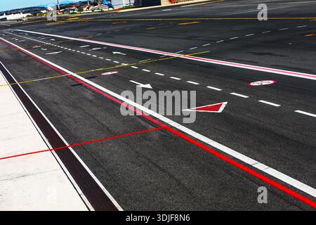 Asphaltfläche des Flughafens mit deutlichen Markierungen und Richtungspfeilen. Flugzeuge sind im Hintergrund geparkt. Start- und Landebahnoberfläche mit regulatorischem airp Stockfoto