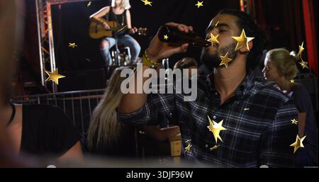 Trinkender bärtiger Mann in kariertem Hemd, der braune Bierflasche in einem kleinen Live-Veranstaltungsort hebt, Akustikgitarre Stockfoto