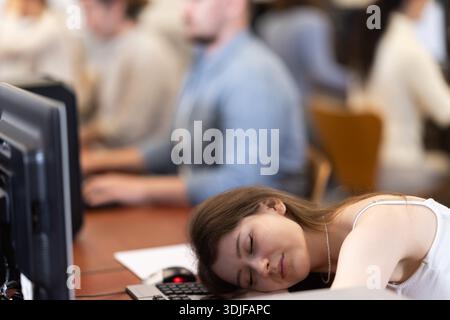 Junge Studentin schläft während der Fortbildung im Computerlabor ein Stockfoto