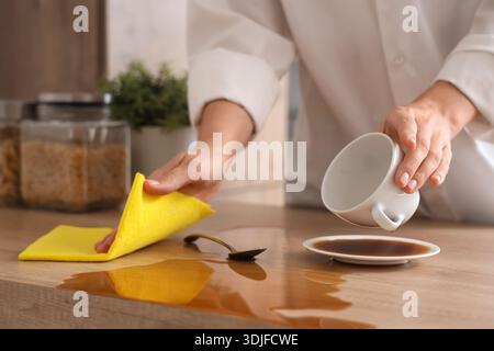 Frau, die mit einem Lappen verschütteten Kaffee auf dem Tisch in der Küche abwischt, Nahaufnahme Stockfoto