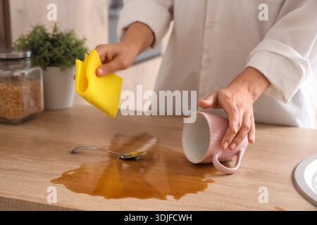 Frau, die mit einem Lappen verschütteten Kaffee auf dem Tisch in der Küche abwischt, Nahaufnahme Stockfoto