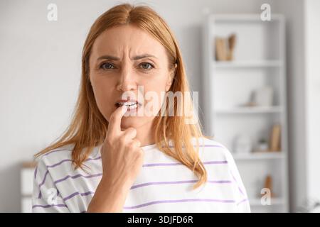 Besorgte reife Frau beißt zu Hause Nägel Stockfoto