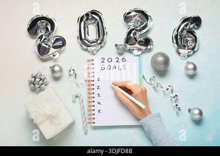 Frau mit Figur 2026, Geschenkbox und Weihnachtsdekor, die To-do-Liste auf farbigem Hintergrund schreibt Stockfoto