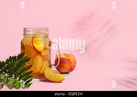 Glas leckerer Pfirsicheistee auf rosa Hintergrund, Nahaufnahme Stockfoto