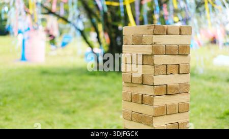 Der Holzblockturm steht auf grünem Gras mit bunten Bändern, die an Ästen hängen, und verschwommenen Objekten, die im Außenbereich sichtbar sind Stockfoto
