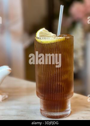 Hohes Glas Eistee mit Zitronenkeil und Stroh auf Marmoroberfläche in gemütlicher Inneneinrichtung. Stockfoto