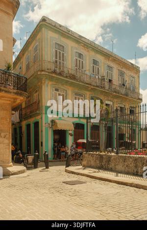 Havanna, Kuba 2024. April 15 – an einer Straßenecke in Old Havanna steht Ein pastellfarbenes Kolonialgebäude, während sich die Besucher unter der verwitterten Fassade Re versammeln Stockfoto