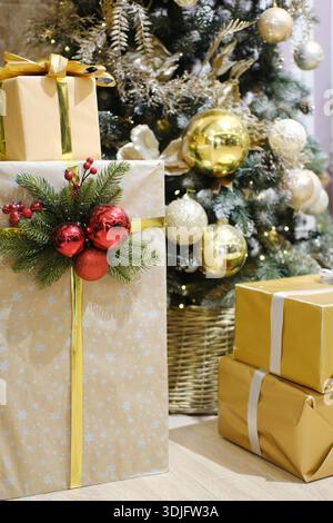 Wunderschön gewickelte Geschenke in Gold und Silber, verziert mit festlichen Elementen, sind neben einem Weihnachtsbaum platziert, was den fröhlichen Feiertag am Vormittag unterstreicht Stockfoto