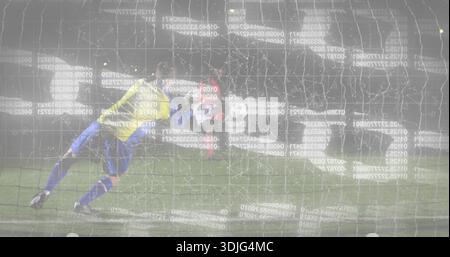 Torhüter in gelbem Trikot, der auf dem Nachtfeld nach links reicht, mit Netz, Ball, Handschuhen und Code-Overlay Stockfoto