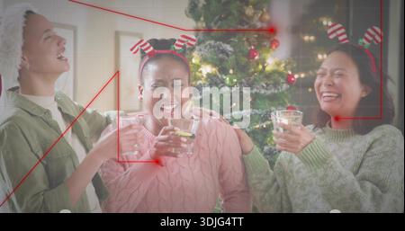 Lächelndes Trio mit gestreiften Haarbändern und kuscheligen Stricken, hält die Brille in der Nähe des beleuchteten Baumes im Wohnzimmer Stockfoto