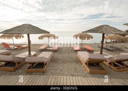 Leerer Strand mit Sonnenliegen und Strohschirmen bei Sonnenaufgang Stockfoto