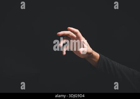 Nahaufnahme einer Hand in dramatischer Pose, die eine Geste oder ein Zeichen macht, um etwas auf einem dunklen Hintergrund zu erreichen, ein symbolisches Zeichen, das das Konzept von zeigt Stockfoto