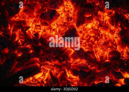 Brennende Kohlen im Dunkeln, schwelende Kohle. Leuchtend rote Feuerfunken. Hintergrund. Stockfoto