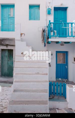 Eine Katze ruht auf weißen Treppen, eine andere bewegt sich durch blaue Türen Folegandros Stockfoto