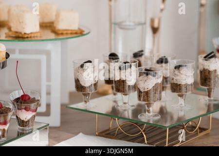 Ein luxuriöses Dessertaufstrich mit Mini-Oreo-Käsekuchen in Glasbechern und weißem Milchgebäck auf Ständen aus Glas, ideal für Hochzeiten, PA Stockfoto