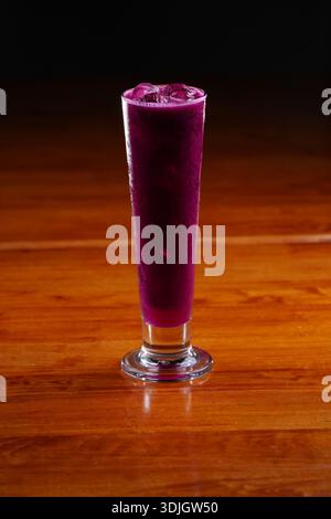 Tiefvioletter Frucht-Smoothie mit eiskalter Textur, hoch in einem klaren Glas serviert, das lebhafte Farben und gekühlte Konsistenz betont. Stockfoto