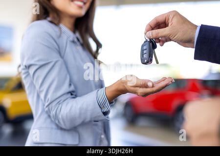 Eine junge weiße Frau kauft ein Auto in einem Autohaus. Der Verkäufer gibt die Autoschlüssel. Lächelnder Verkäufer oder Manager, der der modernen glücklichen Frau, die neu ist, Autoschlüssel gibt Stockfoto
