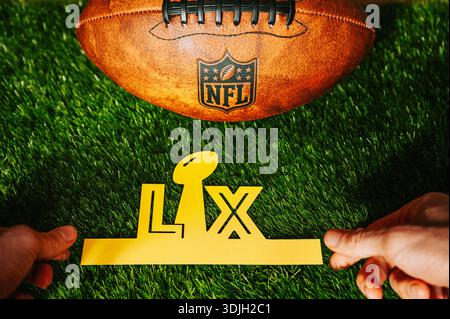 Hände halten LX-Buchstaben neben einem American Football mit Seattle Seahawks und New England Patriots Logos auf grünem Gras, Super Bowl LX in Levi’s Sta Stockfoto