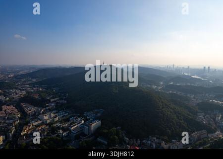 Ein panoramablick aus der vogelperspektive zeigt eine große Stadt in China, mit einem üppigen grünen Berg, der über seinen modernen Gebäuden und einer ruhigen Landschaft thront. Stockfoto
