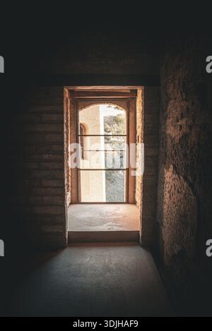 Blick auf ein helles Licht, das durch eine bogenförmige Tür in einem dunklen, steinernen Raum leuchtet und die Außenwelt von Granada, Andalusien, Spanien beleuchtet. Stockfoto