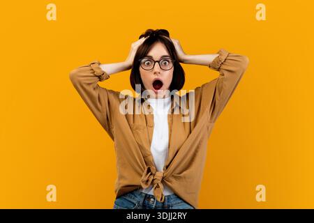 Unglaubliche Nachrichten. Schockierte Frau, die ihren Kopf schockiert über den gelben Studiohintergrund berührt, kann es nicht glauben, ein unglaubliches Angebot zu machen Stockfoto