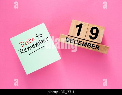 Haftnotiz neben einem Holzblock-Kalender, der den 19. Dezember auf rosa Hintergrund zeigt Stockfoto