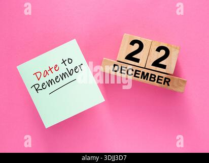 Haftnotiz neben einem Holzblock-Kalender, der den 22. Dezember auf rosa Hintergrund zeigt Stockfoto