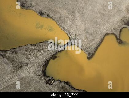 Aus der Vogelperspektive auf das Land trifft auf das Wasser und schafft einen starken Kontrast zwischen den Erdtönen und den goldenen Tönen des Wassers, Selfoss, Island. Stockfoto