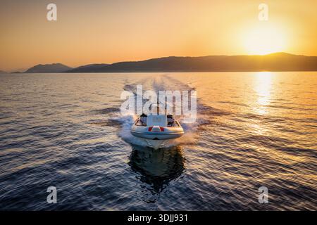 Vorderansicht eines RIB-Motorbootes, das während eines goldenen Sonnenuntergangs im Sommer über das ruhige Meer fährt Stockfoto